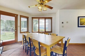 Ein Essbereich mit Holztisch und -stühlen, einem Deckenventilator und großen Fenstern.