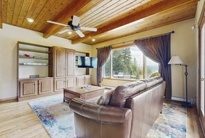 Ein Wohnzimmer mit einer Couch, Holzboden, Fernseher und großen Fenstern.