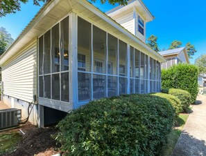 A two-story house with a covered porch, a small attached garage, and a well-maintained hedge. - House #20 Sunshine Cottage (Not Pet Friendly) (Leesburg)
