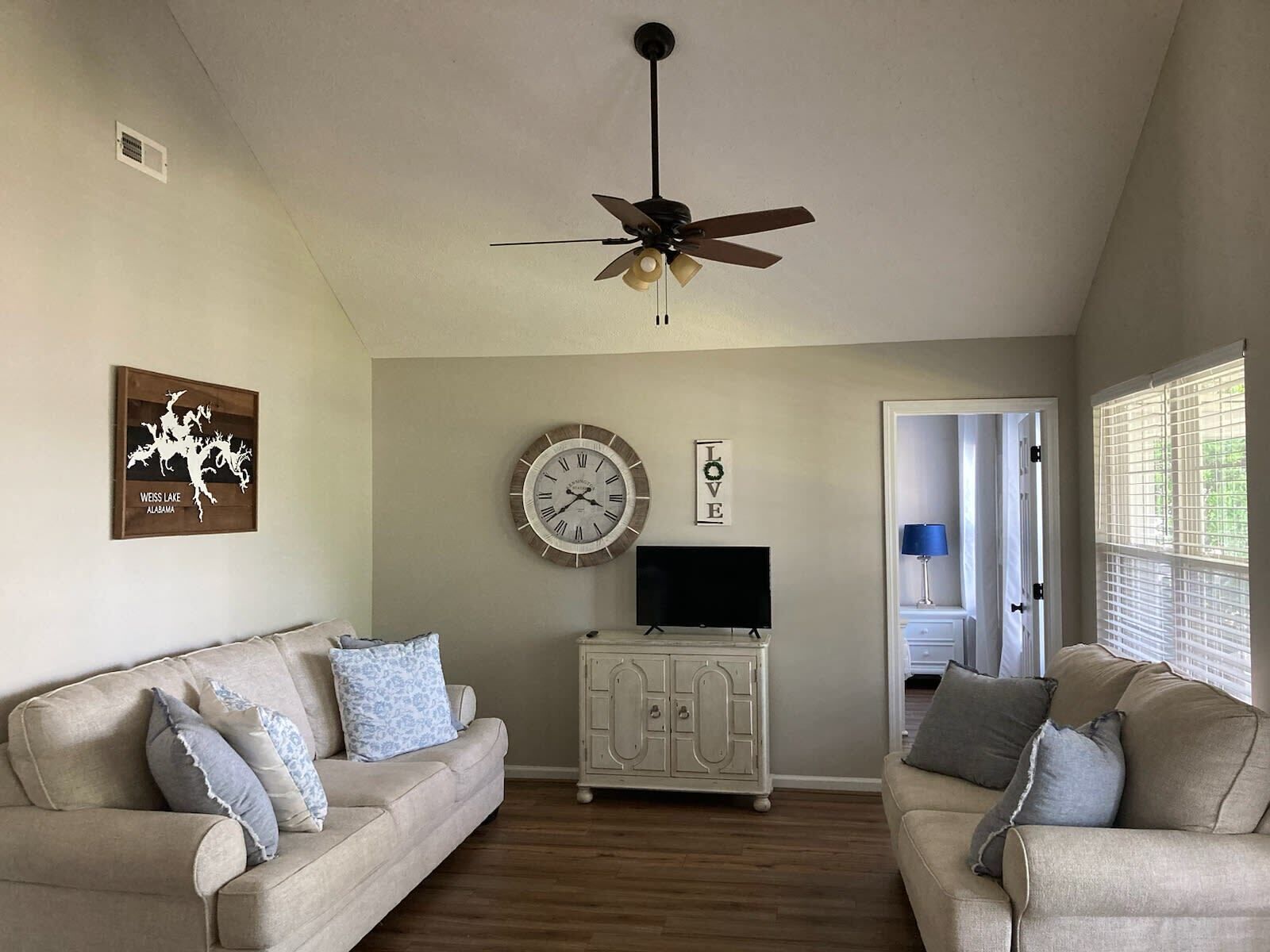A living room with two sofas, a ceiling fan, a clock, a TV, and a cabinet.