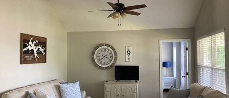 A living room with two sofas, a ceiling fan, a clock, a TV, and a cabinet.