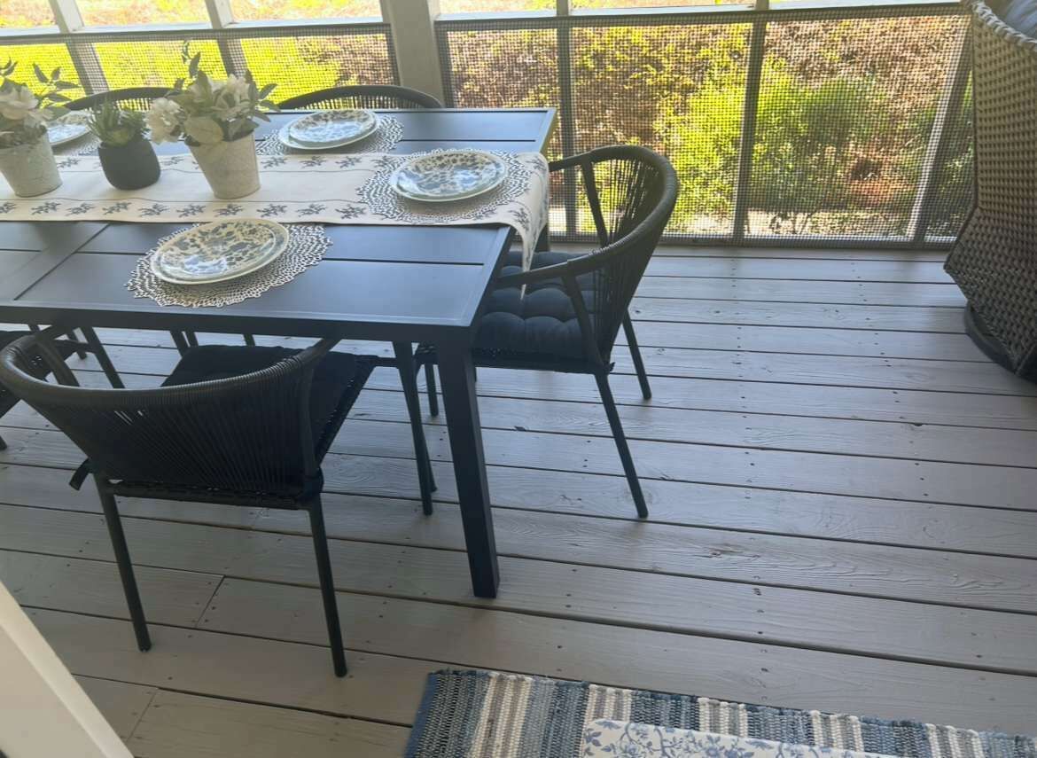 A wooden deck with a table set for four, surrounded by chairs, and potted plants on the table.