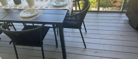 A wooden deck with a table set for four, surrounded by chairs, and potted plants on the table.