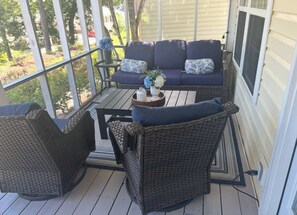 A covered porch with wicker furniture, a blue sofa with patterned cushions, and a small table with a vase. - House #20 Sunshine Cottage (Not Pet Friendly) (Leesburg)