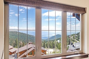 Großes Fenster mit Blick auf eine gebirgige Landschaft, Holzhütten und einen klaren Himmel.