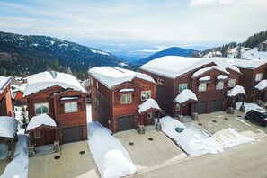 Eine Gruppe Holzhütten mit schneebedeckten Dächern, eine Auffahrt und eine Bergkulisse.