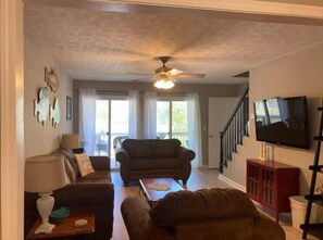A living room with a ceiling fan, a sofa, a coffee table, and a TV mounted on the wall. - 25 Sweet Serenity - Weiss Lake (Leesburg)