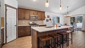 A modern kitchen with wooden cabinets, a central island with stools, stainless steel appliances, and pendant lighting.