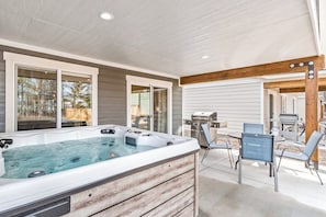 Un jacuzzi con revestimiento de madera, un patio con sillas y una parrilla.