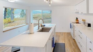 A modern kitchen with a large island, white cabinetry, and a view of a natural landscape. - Charming home with river views, spacious patio, BBQ, WiFi and streaming (Sandpoint)