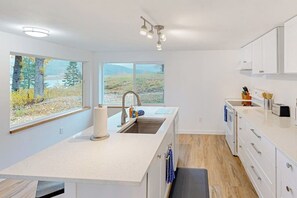 Eine moderne Küche mit einer großen Kochinsel, weißen Schränken und Blick auf eine natürliche Landschaft.