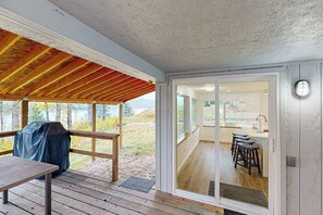 Ein überdachter Außenbereich mit Holzterrasse, Grill und Blick auf eine Küche mit Barhocker.