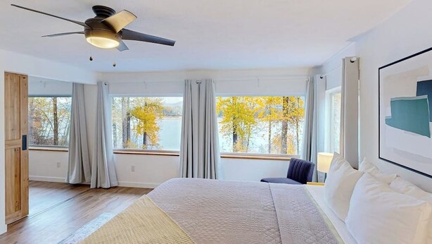 A bedroom with a bed, a ceiling fan, a window with curtains, and a view of trees. - Charming home with river views, spacious patio, BBQ, WiFi and streaming (Sandpoint)