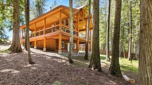 Een houten vakantiehuis met meerdere verdiepingen en een terras, omringd door bomen.