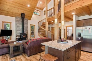 Ein modernes Interieur mit Kamin aus Stein, einer Holztreppe und einer Küche mit Edelstahlgeräten.