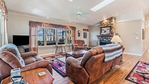 Ein Wohnzimmer mit einer Couch, Sesseln, einem Couchtisch, einem Fernseher und einem Kamin.