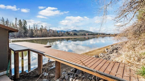 Eine Holzterrasse erstreckt sich über einen ruhigen See, umgeben von Bäumen und Hügeln.