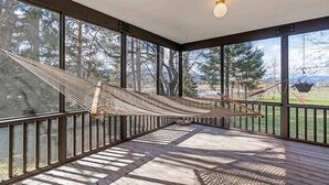 Eine überdachte Veranda mit einer Hängematte, großen Fenstern und Blick auf Bäume und Berge.