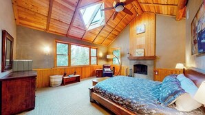 Een slaapkamer met een schuine kap, een bed, een open haard en grote ramen.