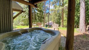 Een hottub met een houten terras, omringd door bomen en een heldere lucht.