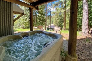 A hot tub with a wooden deck, surrounded by trees and a clear sky.
