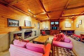 L’intérieur d’un chalet chaleureux, avec des murs en bois, une cheminée, un canapé et une bibliothèque.