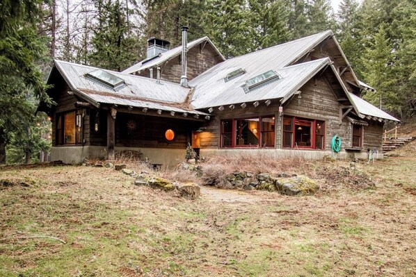 A rustic cabin with a steep roof, large windows, and a stone foundation.