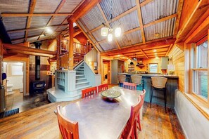 A spacious cabin interior with a dining area, kitchen, and a staircase leading to a loft.