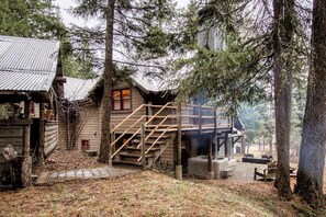 Eine rustikale Holzhütte mit einer Holztreppe, einem Whirlpool und einer Terrasse, umgeben von Bäumen.