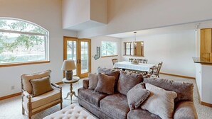 A spacious living room with a large window, a dining area, and a loft space. - Riverfront home with mountain view, hot tub, deck, WiFi, W/D, & fireplace (Sagle)