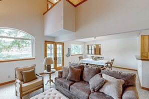 A spacious living room with a large window, a dining area, and a loft space. - Riverfront home with mountain view, hot tub, deck, WiFi, W/D, & fireplace (Sagle)