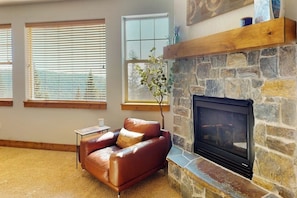 Ein Wohnzimmer mit Kamin aus Stein, einer Ledersofa und großen Fenstern mit Jalousien.
