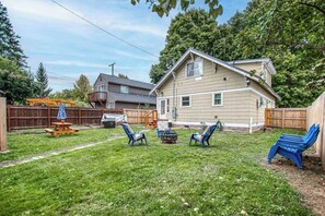 A backyard with a wooden deck, a picnic table, and blue lawn chairs. - 2-story downtown home near the water with firepit, enclosed backyard, fireplace (Sandpoint)