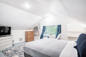 Een slaapkamer met een bed, een televisie, een bureau en een raam met gordijnen.