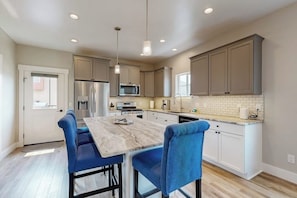 A modern kitchen with a marble countertop, stainless steel appliances, and blue upholstered chairs.