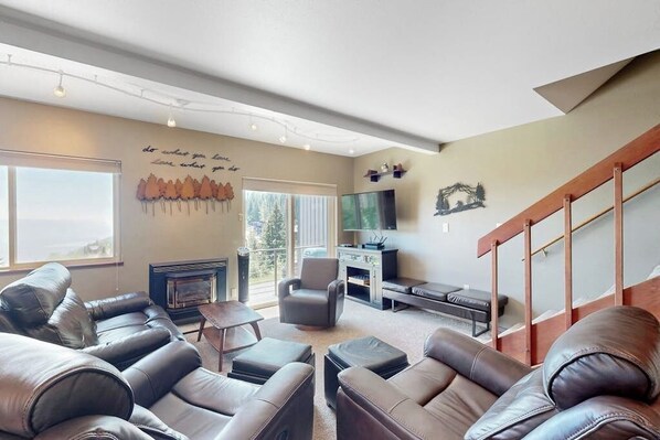 A living room with leather sofas, a fireplace, a television, and a staircase. - Cozy mountain condo with beautiful ski view - Ski In/Ski Out (Sandpoint)