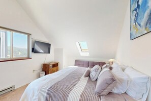 A bedroom with a bed, a TV, a skylight, and a view of the outdoors. - Cozy mountain condo with beautiful ski view - Ski In/Ski Out (Sandpoint)