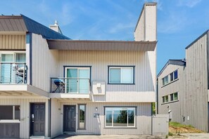 A modern two-story residential building with a balcony, large windows, and a visible garage. - Cozy mountain condo with beautiful ski view - Ski In/Ski Out (Sandpoint)