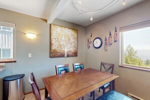 A dining area with a wooden table, chairs, a wall clock, and a window with a view. - Cozy mountain condo with beautiful ski view - Ski In/Ski Out (Sandpoint)