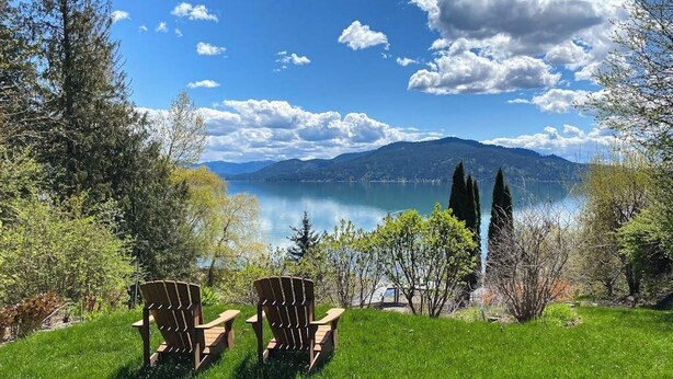 Two Adirondack chairs facing a lake with mountains in the background. - Lakefront home with mtn views, private hot tub, dock, deck, & grill (Sandpoint)