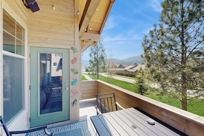 A wooden deck with a table and chairs, a door with a view, and a mountain landscape in the background. - Beautiful condo with river views, deck, BBQ, WiFi, and nearby activities (Sandpoint)