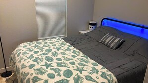 Une chambre à coucher avec un lit, une table de chevet, une lampe et une fenêtre avec des stores.