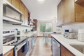 Eine moderne Küche mit Edelstahlgeräten, Holzschränken, einem Essbereich mit Tisch und Stühlen sowie einem großen Fenster für natürliches Licht.