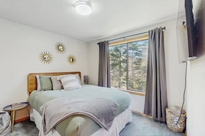Ein Schlafzimmer mit einem großen Bett, einem Nachttisch, einer Lampe, einem Fenster mit Vorhängen und Wanddekorationen.
