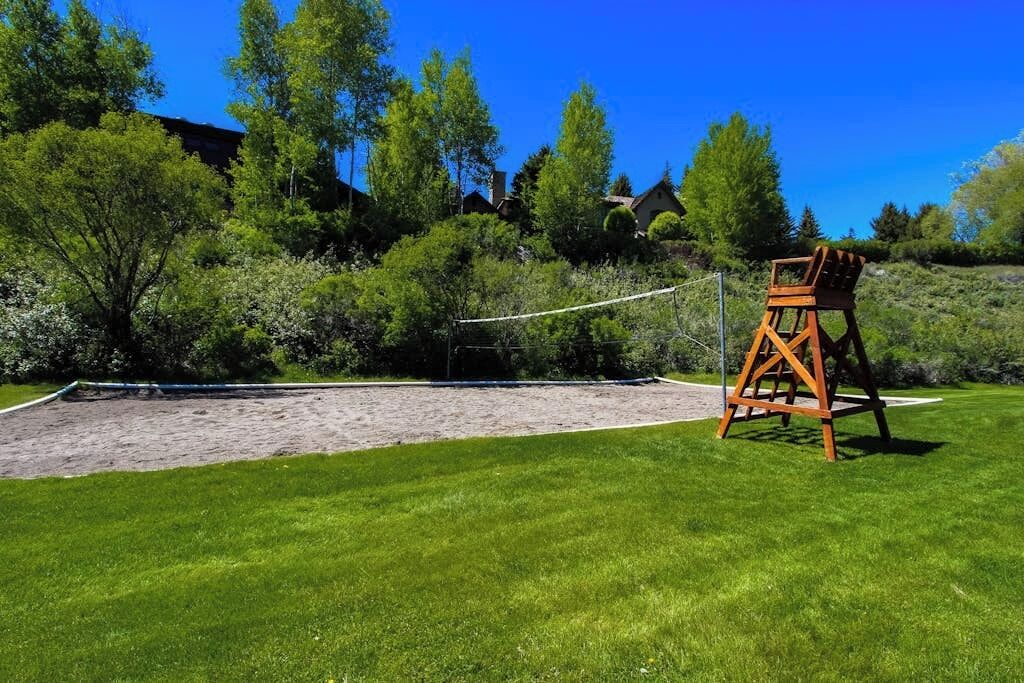 Un terrain de volleyball de sable avec un filet de volleyball en bois, entouré d’une zone herbeuse et d’arbres.
