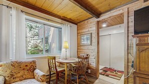 A cozy room with a wooden ceiling, a sofa, a table with chairs, a TV, and a window with curtains. - Convenient Studio, Walking Distance to Sun Valley Lake - Shopping, Skiing Nearby (Sun Valley)