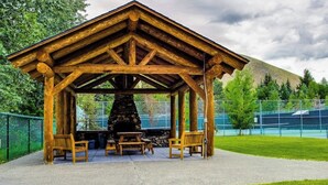 En träbeklädd paviljong med en steneldstad, bänkar och ett stenlagt område.