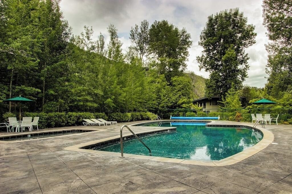 A swimming pool with lounge chairs and umbrellas, surrounded by trees and a house.