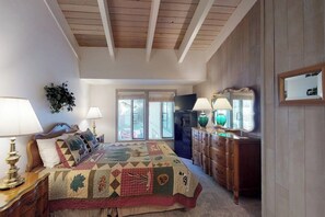 A bedroom with a large bed, wooden ceiling beams, a dresser, and a mirror.