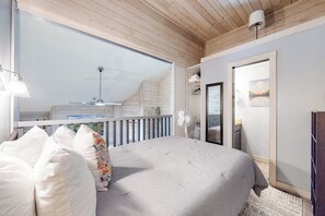 A bedroom with a large bed, a balcony, a fan, and a view of the outdoors.